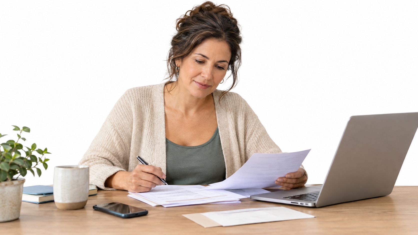 Una mujer adulta trabajando desde casa revisando documentos y usando una computadora portátil en su escritorio.
