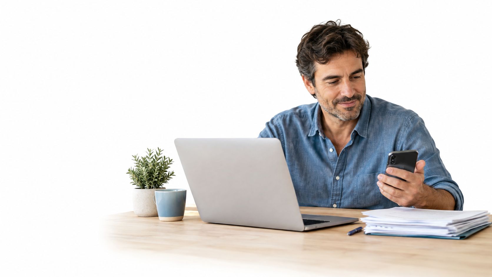 Hombre de mediana edad trabajando con su ordenador portátil y teléfono móvil en un escritorio moderno