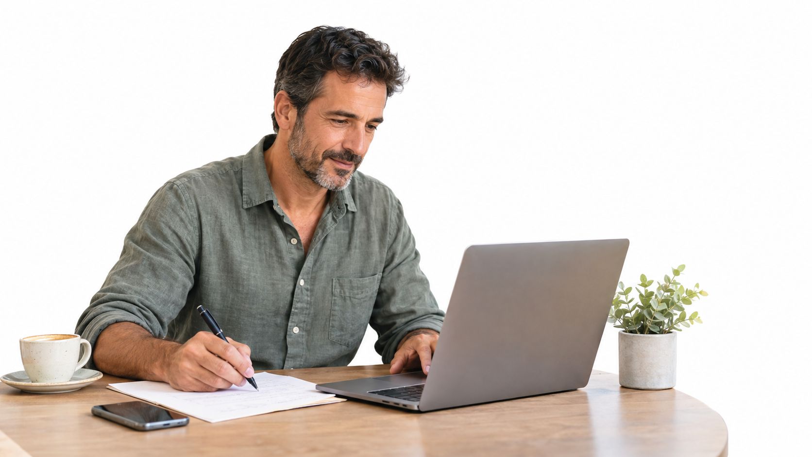 Hombre de mediana edad sentado a una mesa de madera trabajando con una computadora portátil y tomando notas.